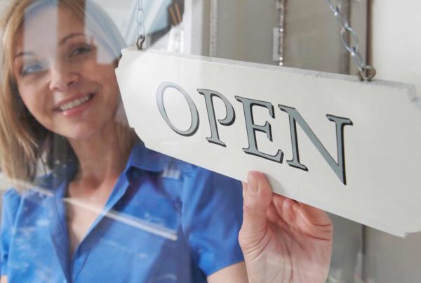 Image of a woman turning a sign notifying her business is open
