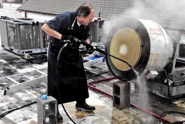 Image of a Halo employee pressure washing a rooftop grease containment system