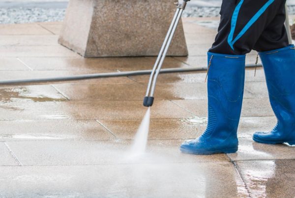 Worker power washing concrete sidewalk