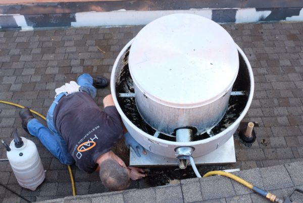 Halo employee scraping grease from rooftop during routine kitchen exhaust cleaning service