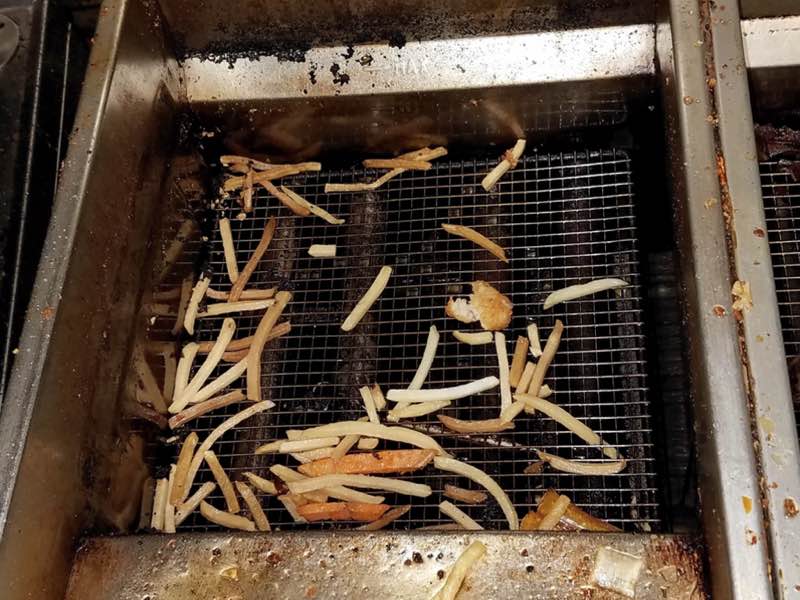 Close-up of dirty fryer with fries and grease